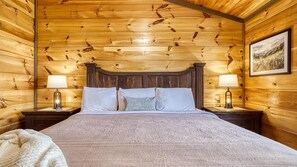 A wooden room with a bed, two bedside lamps, and a framed picture on the wall.