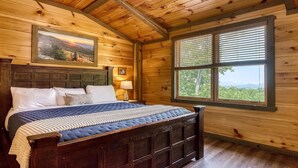 Une chambre dans une cabane en bois, avec un lit, une fenêtre avec des stores et un tableau accroché au mur.