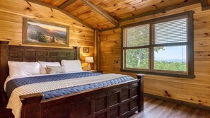 Ein Schlafzimmer einer Holzhütte mit einem Bett, einem Fenster mit Jalousien und einem Gemälde an der Wand.