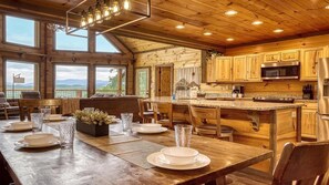 A wooden cabin interior with a dining area, kitchen, and large windows offering a view.