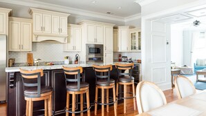 Une cuisine moderne avec des meubles blancs, un îlot central doté de tabourets de bar, des appareils électroménagers en acier inoxydable et un coin repas avec une table et des chaises en bois.