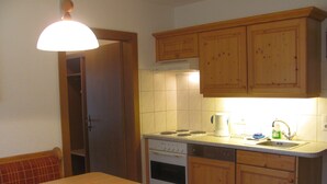 Cozinha compacta com armários de madeira, fogão, pia e mesa de jantar com cadeiras.