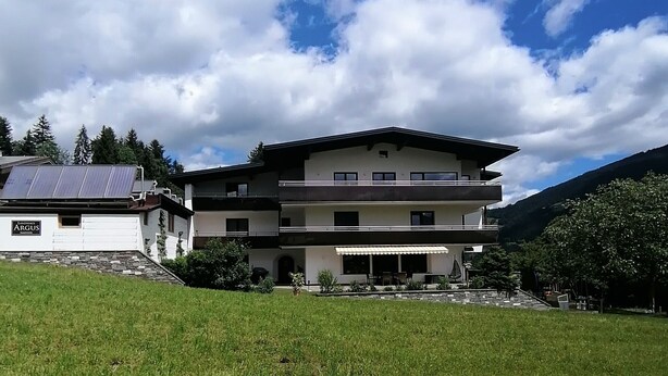 Um edifício de dois andares com telhado plano, painéis solares e uma placa com a inscrição 'ARGUS'.