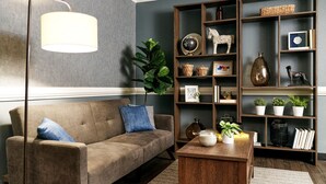 A living room with a sofa, a coffee table, a floor lamp, a bookshelf, and a potted plant. - InTown Suites Extended Stay Newport News VA - North (Newport News)