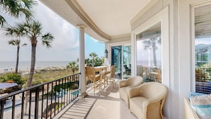 A balcony with wicker furniture, a glass door leading to a pool, and a view of the beach.