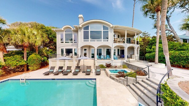 A large, two-story house with a pool, outdoor seating, and a well-maintained garden.