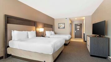 A hotel room with two beds, a TV, a desk, and a door leading to the bathroom.