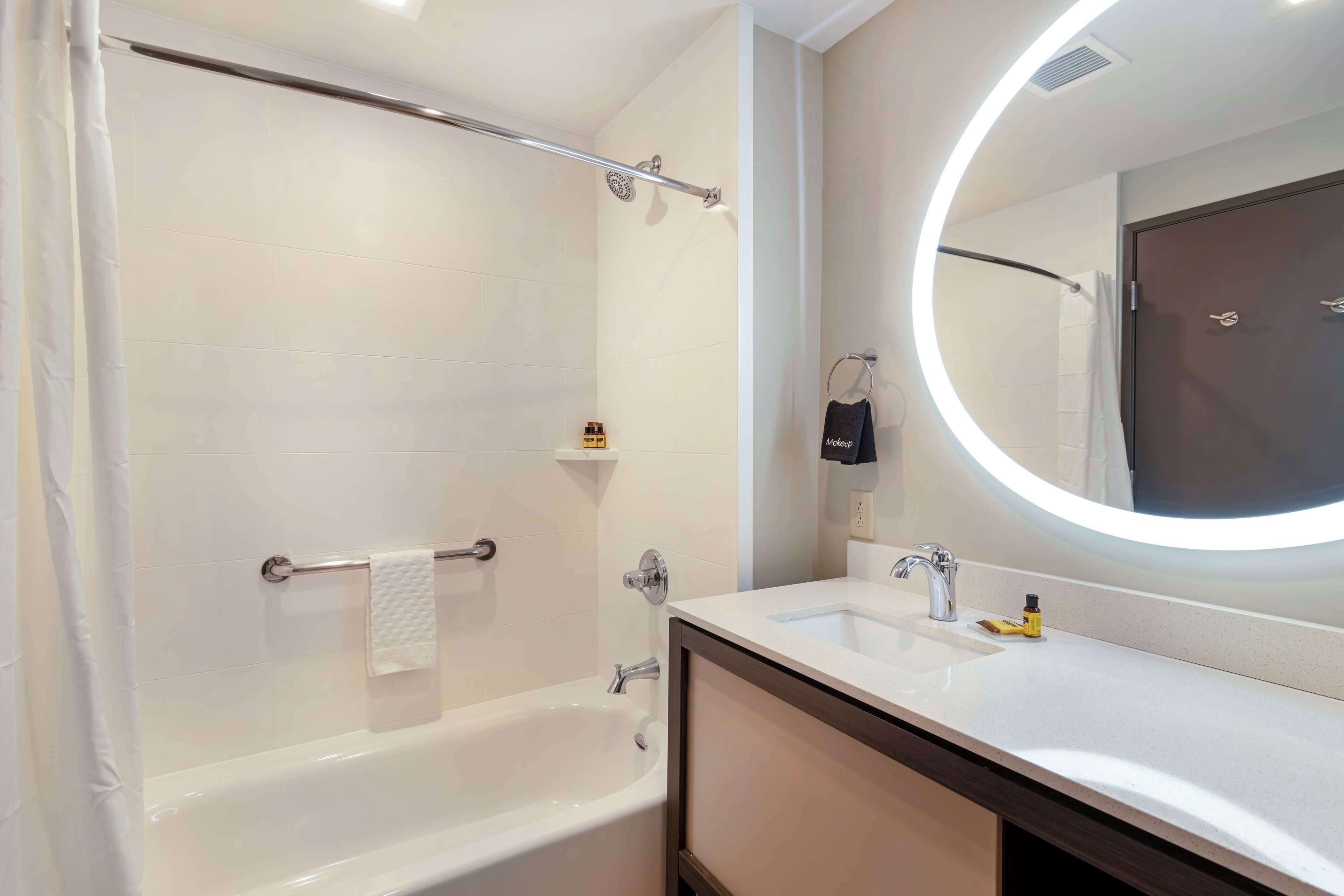 Un baño moderno con bañera, lavabo, espejo con luz circular y perchero para toallas.