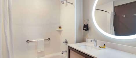 A modern bathroom with a bathtub, a sink, a mirror with a circular light, and a towel rack.