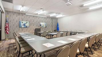 Un salón de conferencias con una larga mesa, sillas, un proyector y banderas.
