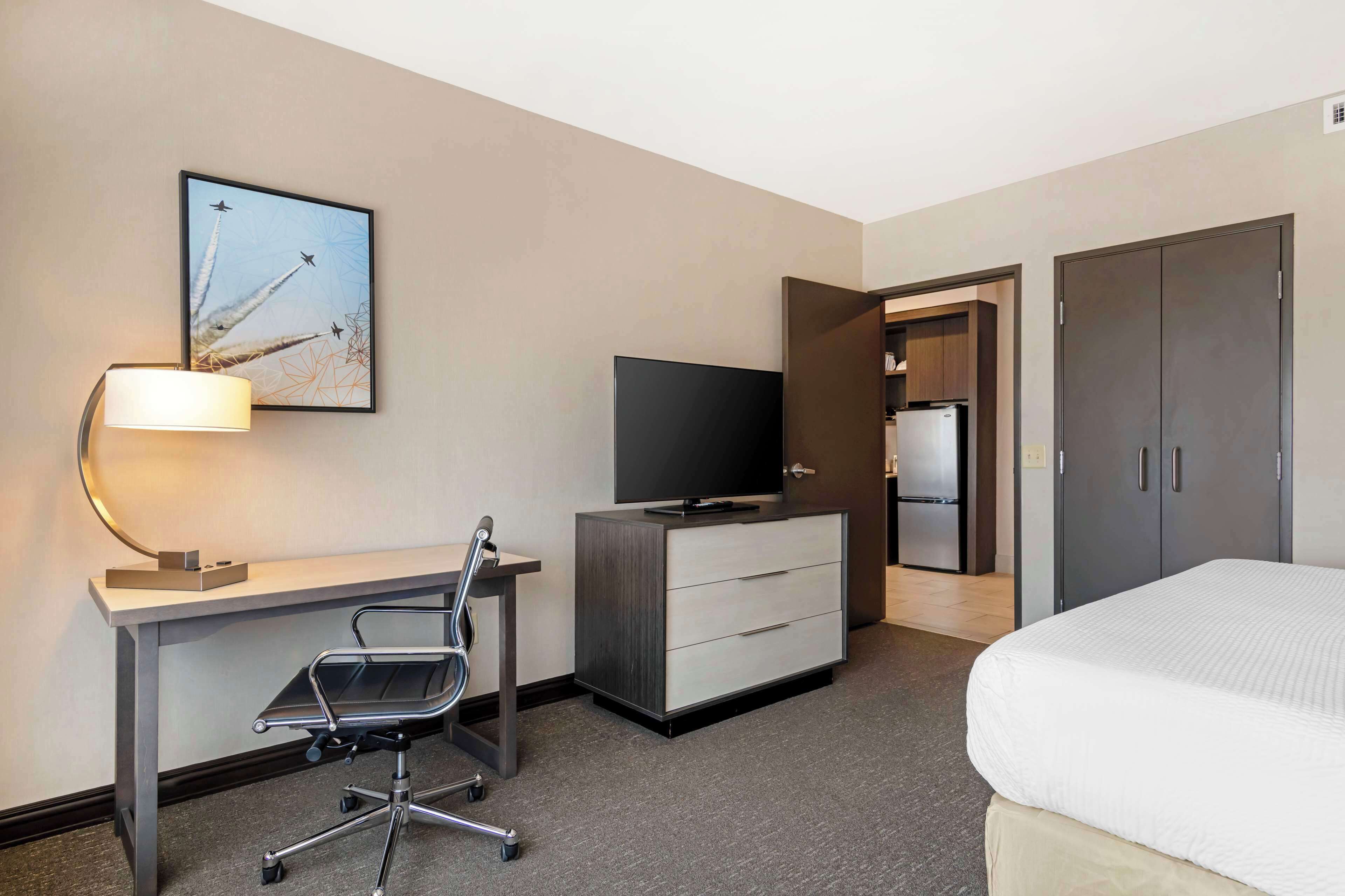Quarto de hotel com escrivaninha, cadeira, televisão, guarda-roupa e cama.