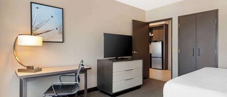 Una habitación de hotel con escritorio, silla, televisor, armario y cama.