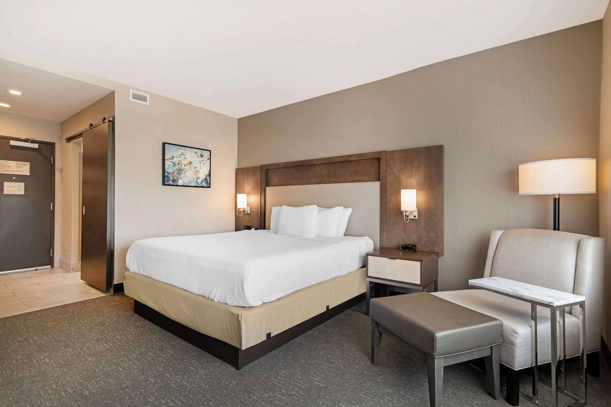 Una habitación de hotel con una cama grande, mesitas de noche, una silla y un banco.