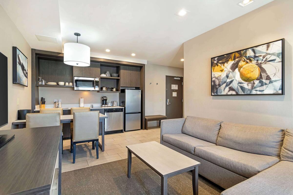 Una sala de estar moderna con un sofá, una mesa de comedor y sillas. Cuenta con una zona de cocina equipada con microondas, estufa y refrigerador.