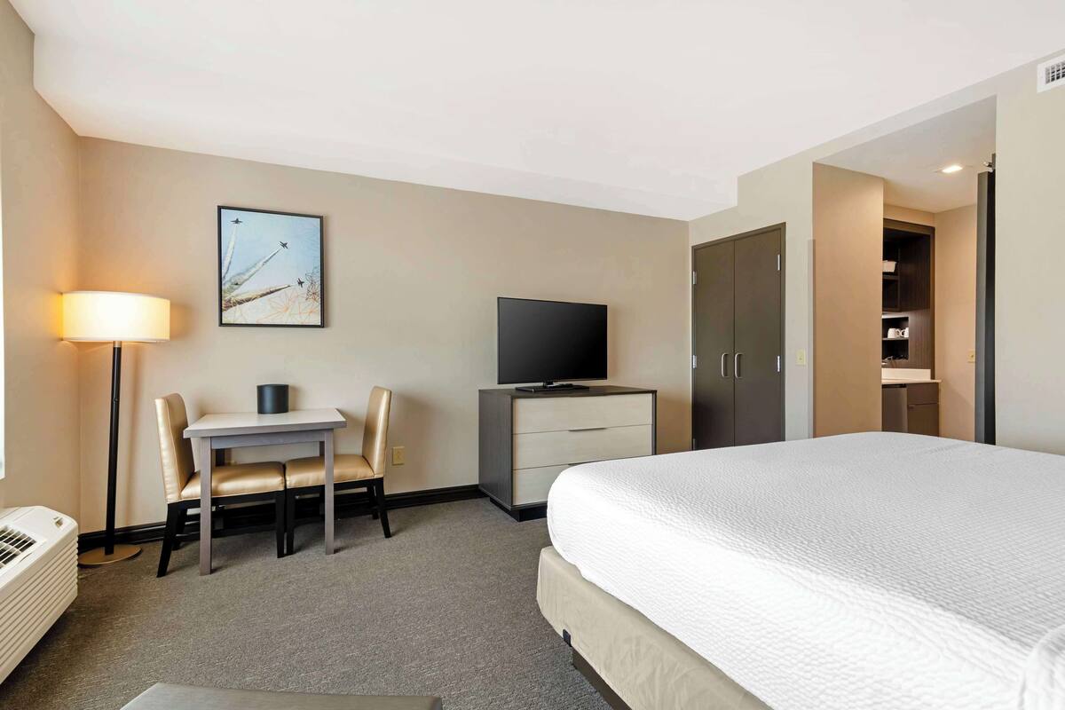 Habitación de hotel con cama, escritorio con silla, televisión, armario y un cuadro en la pared.