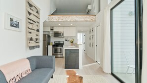 Eine moderne Küche mit Edelstahlgeräten, einer zentralen Kochinsel und einem Essbereich mit grauem Sofa und Holztisch.