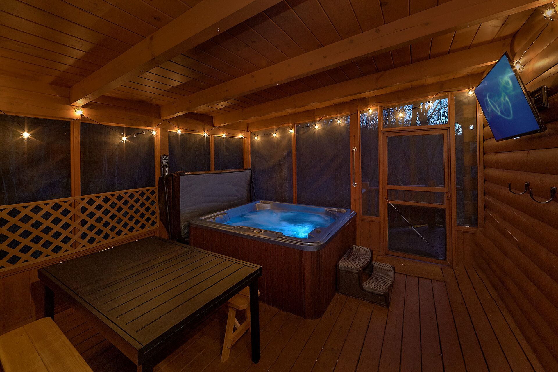 A wooden cabin interior with a hot tub, a table, and string lights.