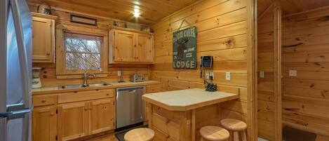 Eine Küchenzeile im Chalet-Stil mit Holzausstattung, einem Edelstahlkühlschrank, einem Geschirrspüler, einer Bar mit Hockern und einem Schild, das eine Lodge bewirbt.