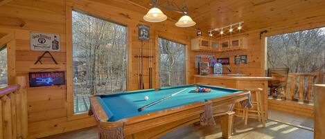 A wooden room with a pool table, billiard cues, and a neon sign.