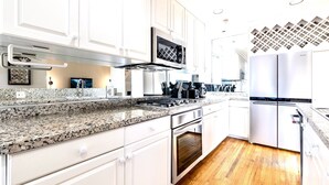 Una cocina moderna con armarios blancos, encimeras de granito, electrodomésticos de acero inoxidable y suelo de madera.