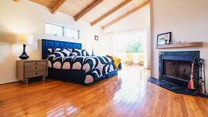 Un dormitorio con una cama grande, suelo de madera, chimenea y vistas al exterior.
