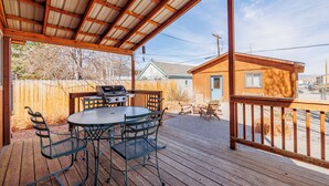 A covered outdoor patio with a grill, metal chairs, and a table.