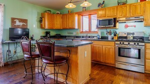 A kitchen with wooden cabinets, a stainless steel stove, a microwave, and a large island with bar stools.