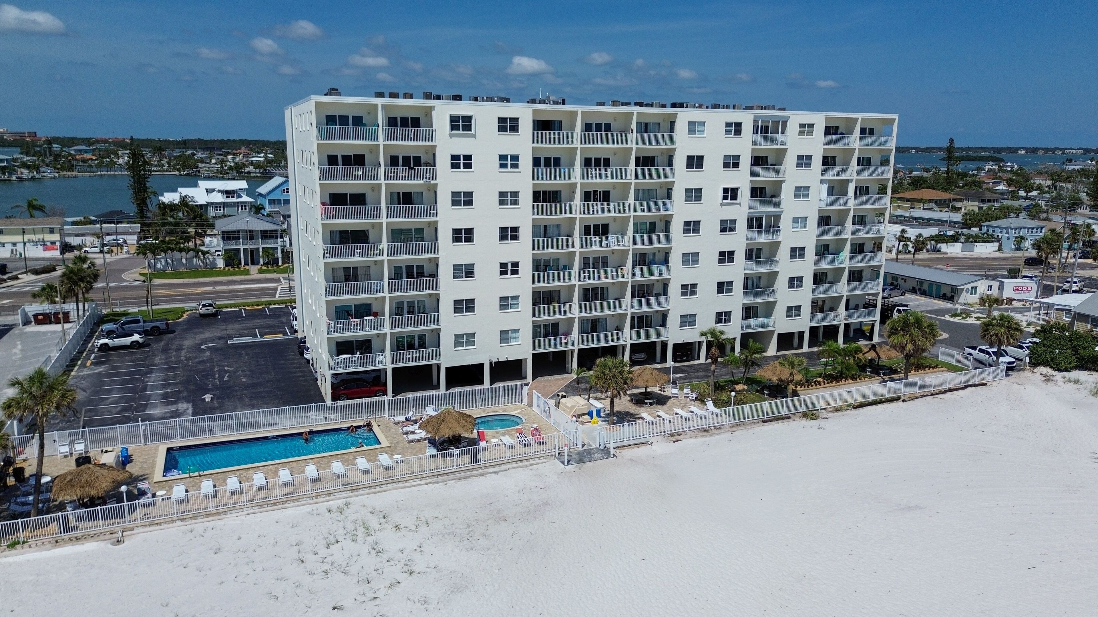 Un hotel de varios pisos con piscina y vista a la playa, con balcones y zona de estacionamiento.
