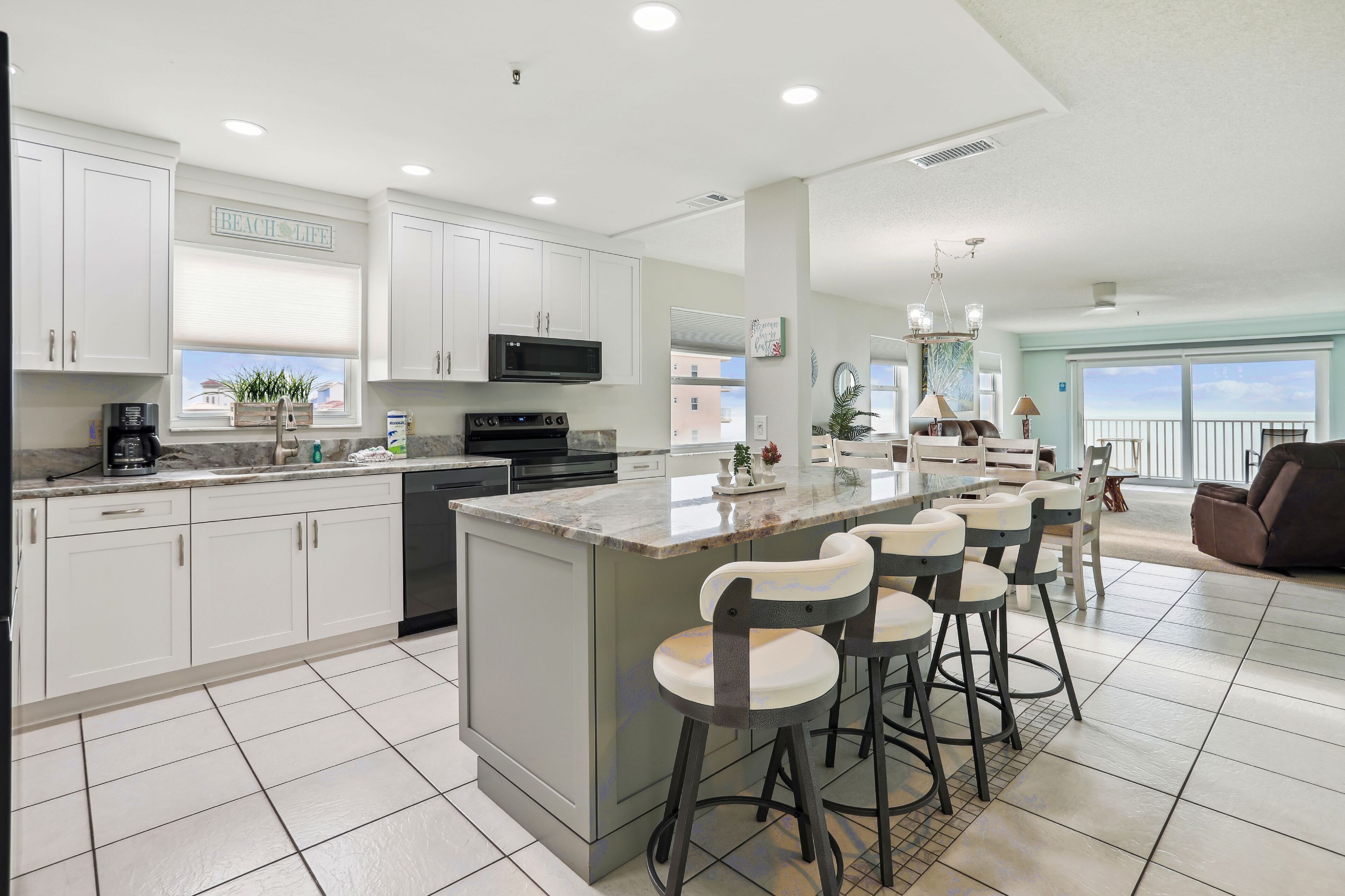A modern kitchen with white cabinets, a large island with bar stools, and a view of the ocean.