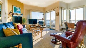 A spacious living room with a large flat-screen TV, a sofa, a red leather chair, and a balcony with a view of the sea. - Unobstructed View Of Monterey Bay! (Aptos)