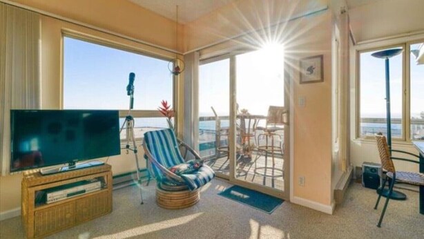A room with a large TV, a striped chair, a dining table, and a balcony with a view of the sea. - Unobstructed View Of Monterey Bay! (Aptos)