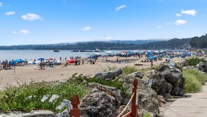 Una spiaggia con ombrelloni e persone, un primo piano roccioso e un cielo sereno.