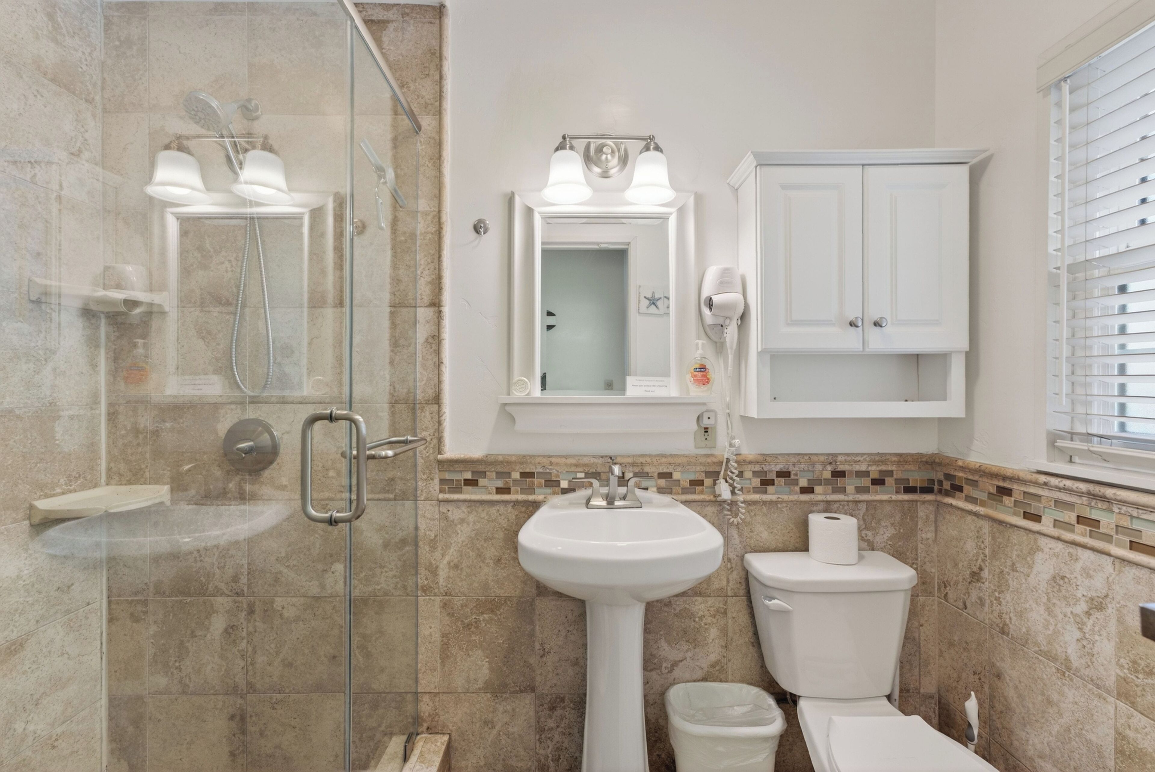 A bathroom with a glass-enclosed shower, a pedestal sink, a toilet, and a cabinet above the sink.