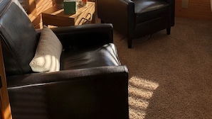 Een gezellig interieur van een chalet met houten wanden, twee leren fauteuils, een tafeltje met een lamp en een decoratief bord.