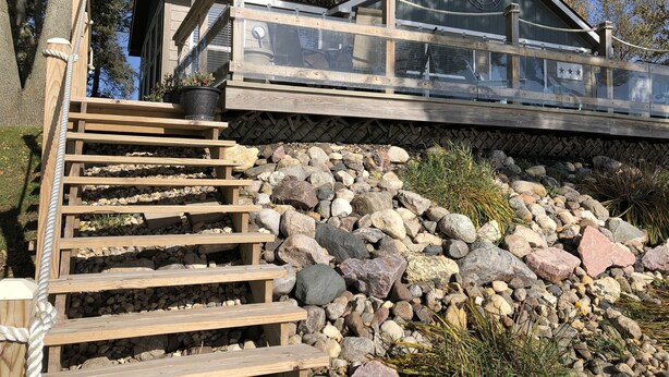 Een houten trap die leidt naar een glazen terras met een fundering van natuursteen.