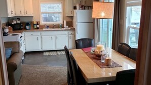 Een kleine keuken met witte kasten, een koelkast, een magnetron en een eethoek met een tafel en stoelen.