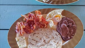 Lautasella on erilaisia aamiaisruokia, kuten pekonia, kananmunia ja tortilloja.