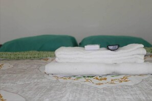 A neatly made bed with white towels and a small white object on top, possibly a remote control, on a bed with a green pillow and a patterned bedspread.