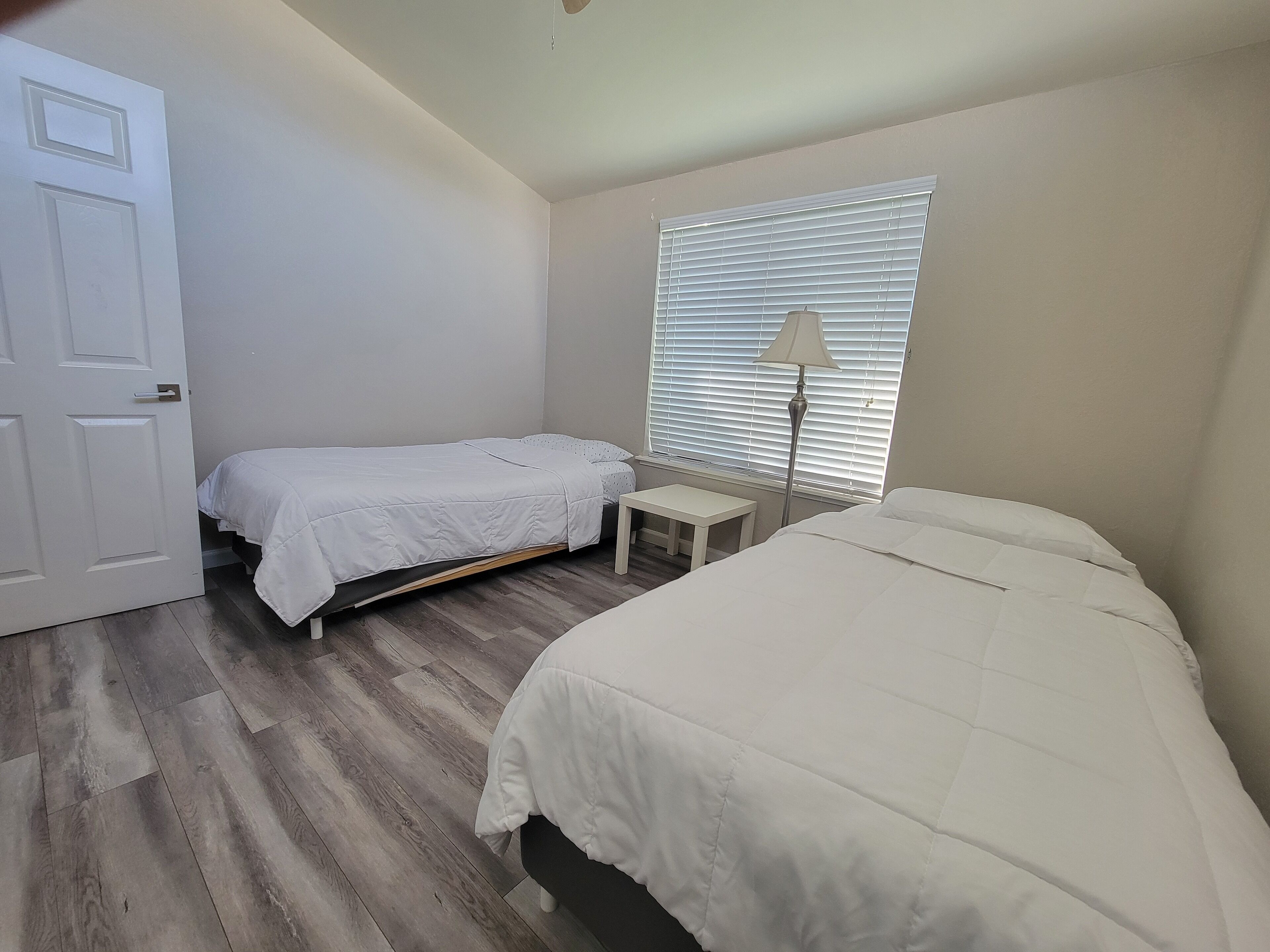 Un dormitorio con dos camas, una mesita de noche, una lámpara y una ventana con persianas.