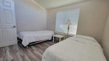 Un dormitorio con dos camas, una mesita de noche, una lámpara y una ventana con persianas.