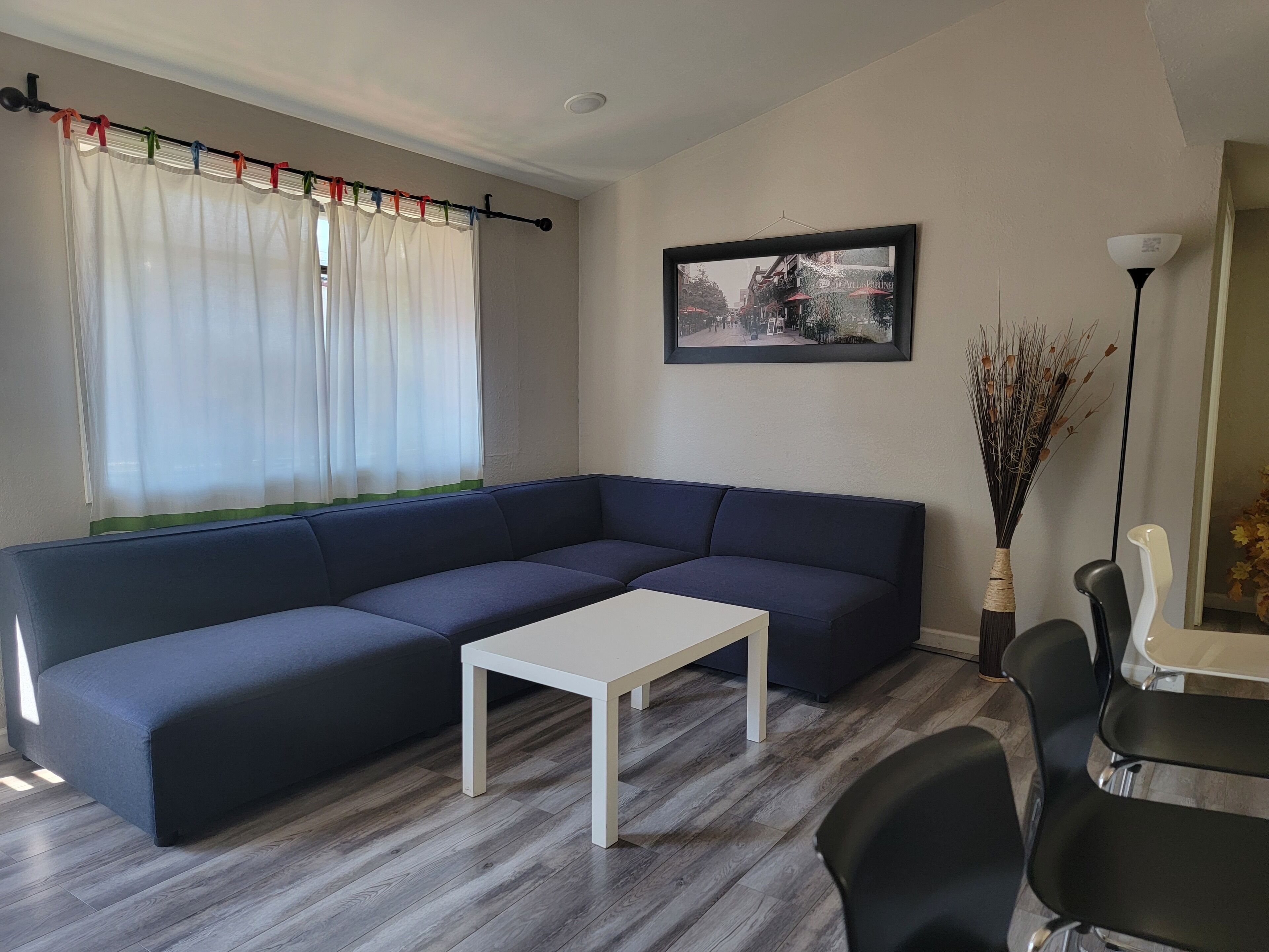 Una sala de estar moderna con un sofá seccional azul oscuro, una mesa de centro blanca y un comedor con una mesa blanca y sillas negras.