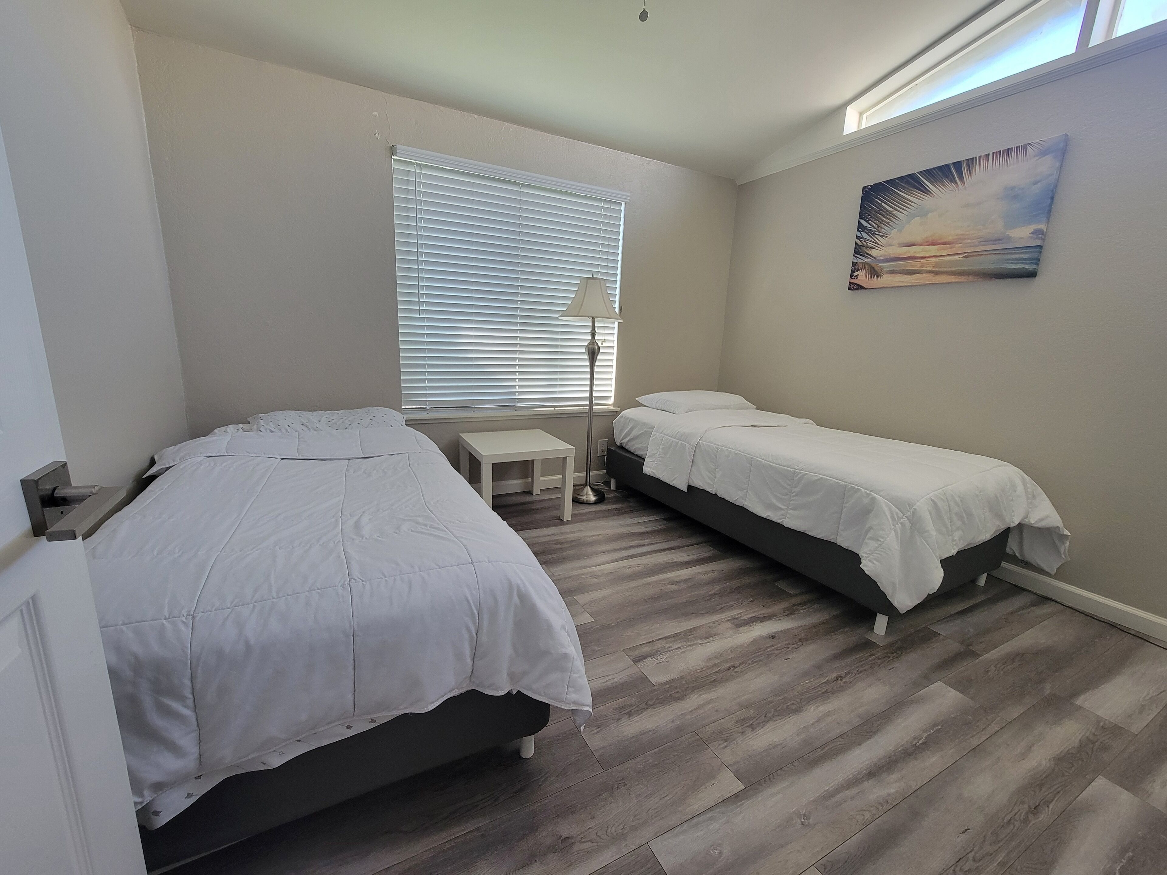 A bedroom with two beds, a small table, and a window with blinds.
