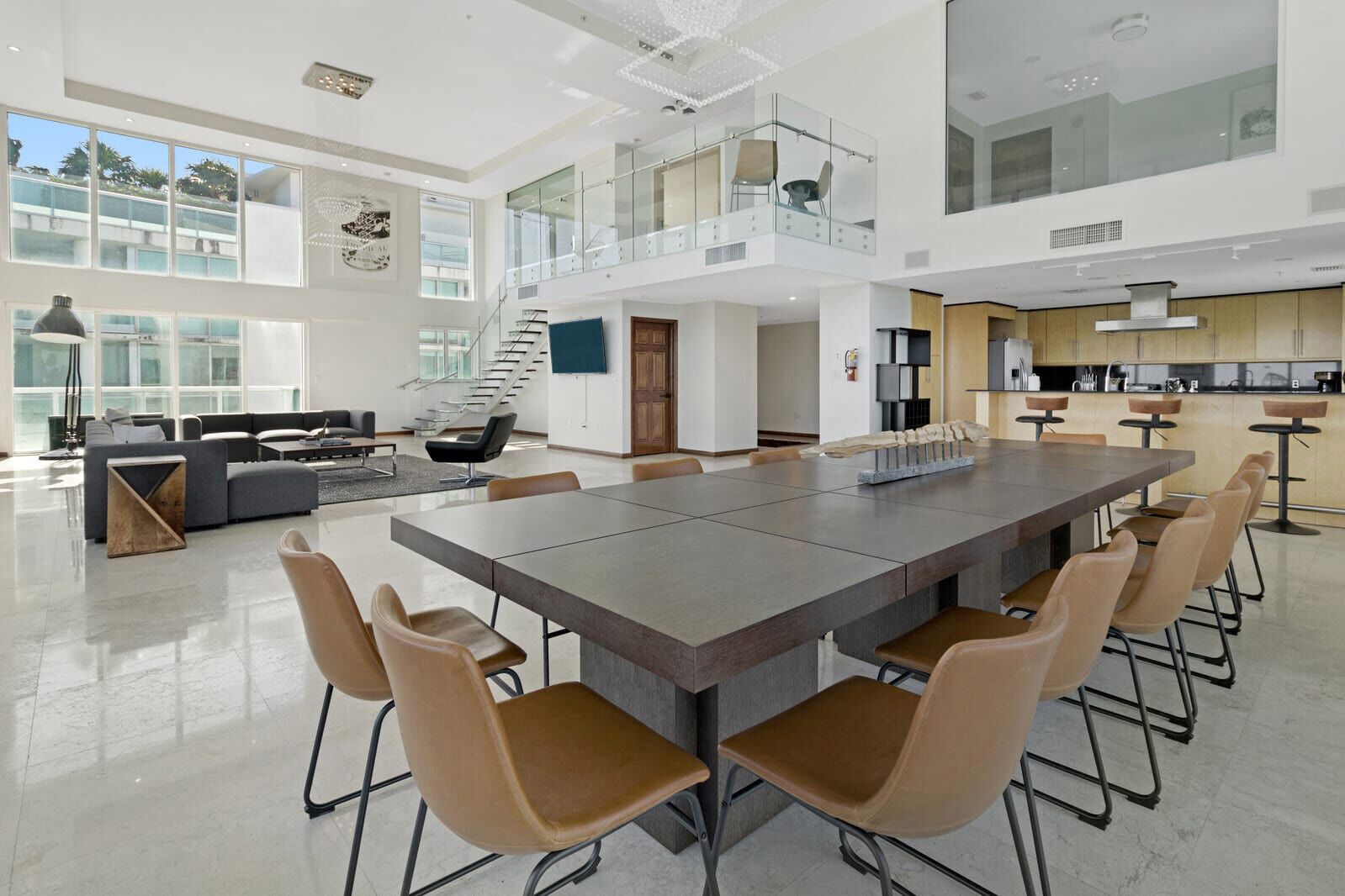 A spacious, modern kitchen with a large island and bar seating, a dining area with a long table, and a living area with a sofa and coffee table.
