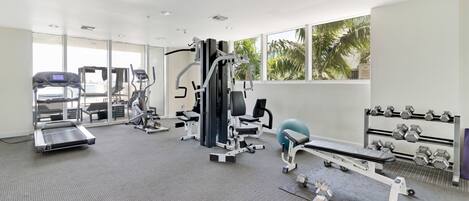 Un gimnasio moderno con máquinas de cardio, equipos de entrenamiento con pesas y mancuernas.