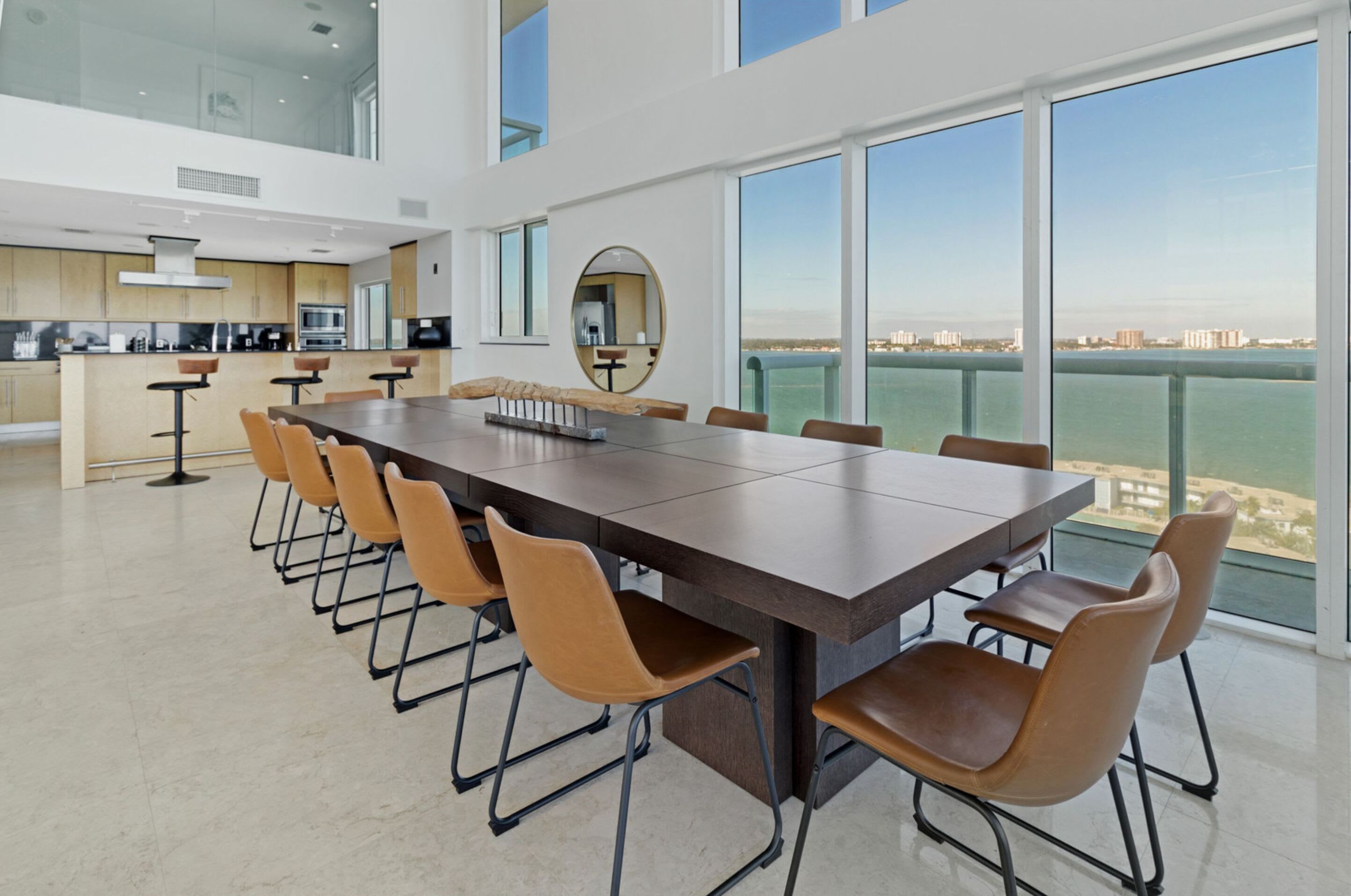 Een moderne keuken met een centraal eiland, een eetgedeelte met een lange tafel en stoelen, en grote ramen met uitzicht op de stad.