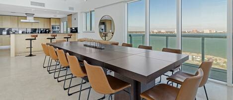 Een moderne keuken met een centraal eiland, een eetgedeelte met een lange tafel en stoelen, en grote ramen met uitzicht op de stad.