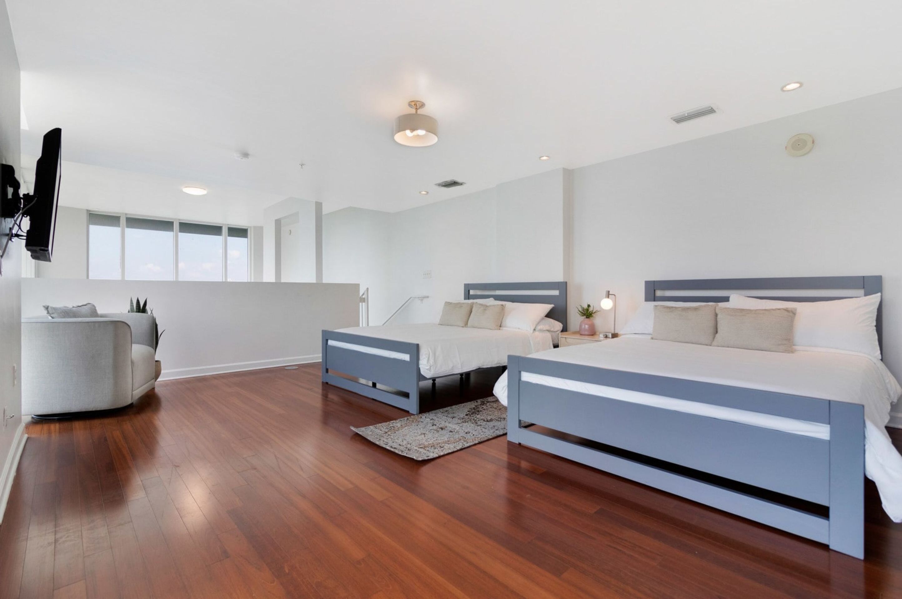 A modern bedroom with two beds, a sofa, and a large window.