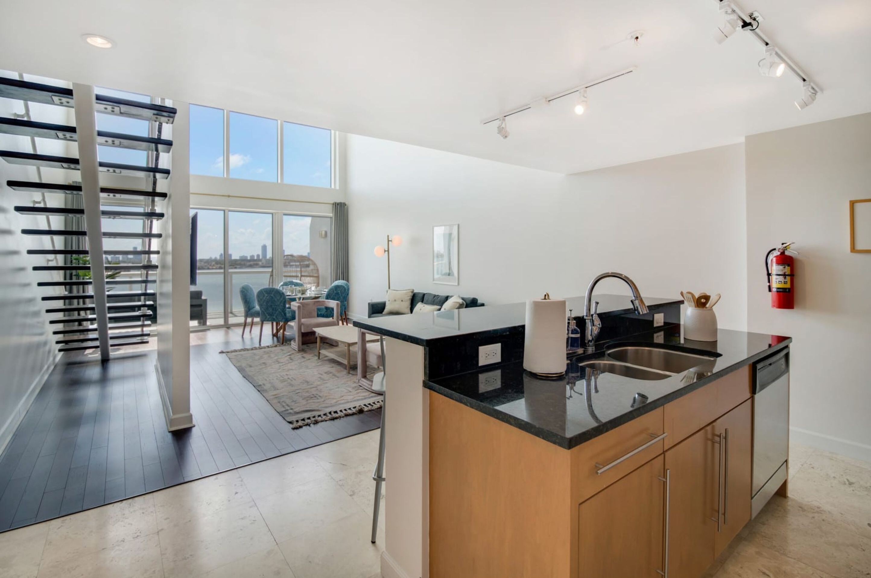A modern kitchen with a large island, a dining area with a view, and a staircase leading to an upper level.