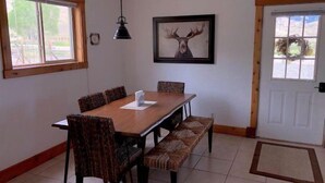 Un coin repas avec une table en bois et des chaises à motifs, un luminaire suspendu et une tête de cerf encadrée accrochée au mur.