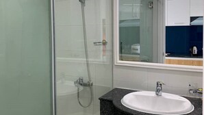 Un baño moderno con cabina de ducha de vidrio, un lavabo blanco con encimera de granito y un espejo grande sobre el lavabo.